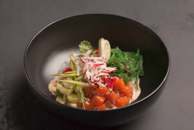 Restoran menüsü. Kırmızı balıklı salata, turp, yosun, avokado, turp, havyar ve yeşillik. Limon soslu. Siyah arka plan. Kabuğun arka planında. Deniz mahsullü siyah tabak. Yeşil, kırmızı, kahverengi, turuncu