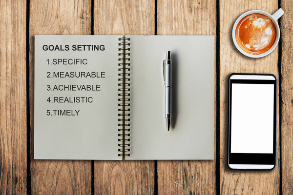 Goal setting as memo on notebook and coffee cup with mobile phon