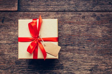 Yukarıda kahverengi hediye kutusu ve kırmızı kurdele ile ahşap backgr etiketi göster