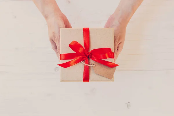 Von oben Hand Frau hält braune Geschenkbox auf weißem Holz Backgro — Stockfoto