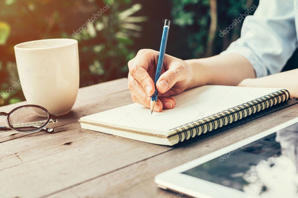 Female hand with pencil writing on notebook. Woman hand with pen