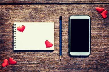 Boş defter, kalem ve telefon bl ile ahşap masa üzerinde kırmızı kalp