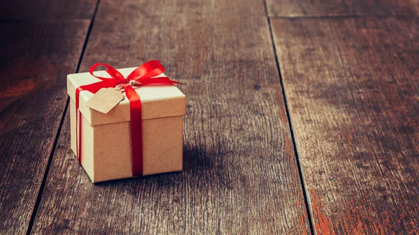 Caja de regalo marrón y cinta roja con etiqueta sobre fondo de madera con s — Foto de Stock