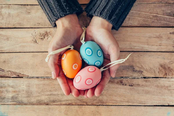 Gros plan main femme tenant et personne Pâques oeufs sur table en bois — Photo