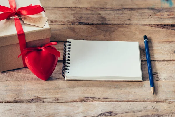 Cuaderno en blanco y caja de regalo con corazón rojo sobre fondo de madera . — Foto de Stock