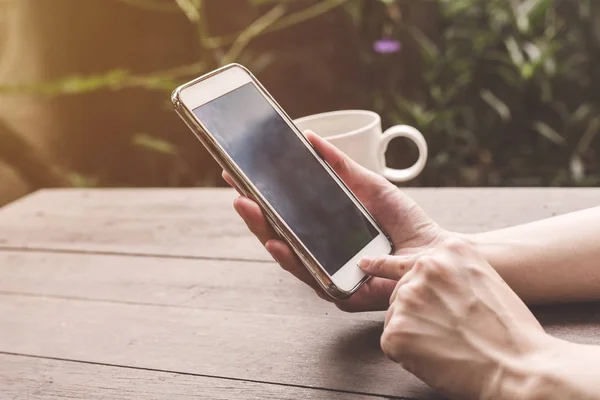 Stäng upp handen kvinna holding och använder telefonen på trä bord med v — Stockfoto