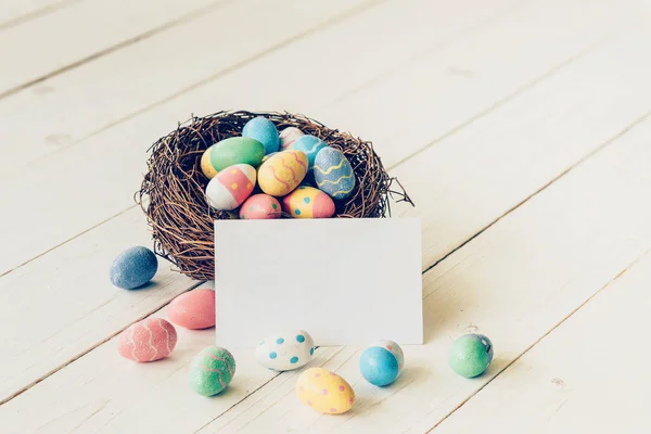 Красочные пасхальные яйца в гнезде и бумажная карточка на деревянном столе ба — стоковое фото