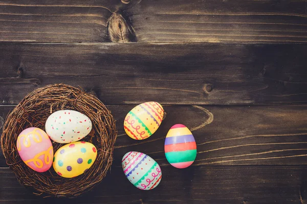 Красочные яйца пасхальные в гнезде на деревянном фоне с кописпа — стоковое фото