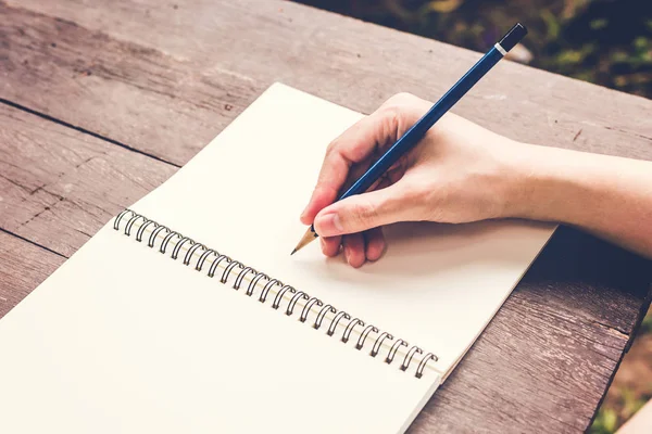 Close up hand woman writing notebook with pencil on wood table. — Stock Photo, Image