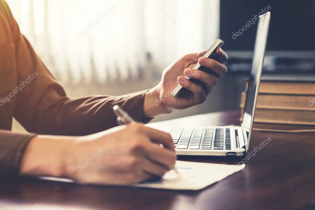 Young business man hand using phone and writing paper in the off