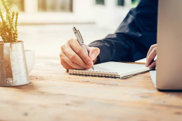 Asia man hand writing notebook paper on wood table in coffee sho