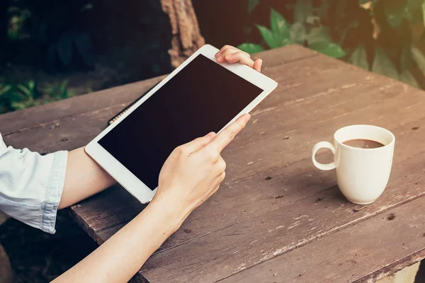 Mulher mão segurando tablet e tela em branco na mesa de madeira — Fotografia de Stock