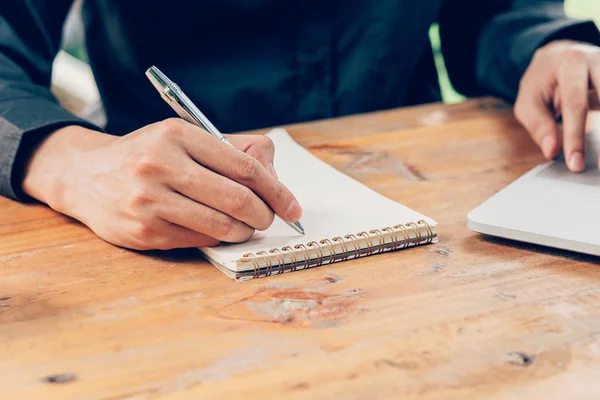 Man hand writing notebook paper and using phone on wood table in