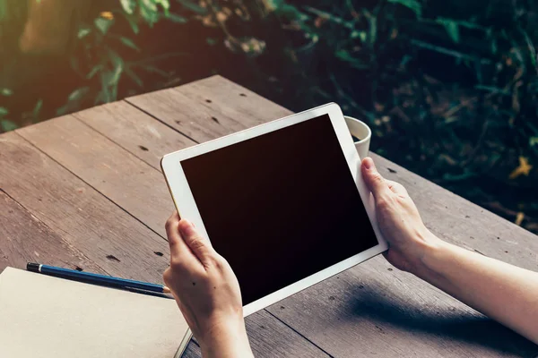 Mulher mão segurando tablet e tela em branco na mesa de madeira — Fotografia de Stock