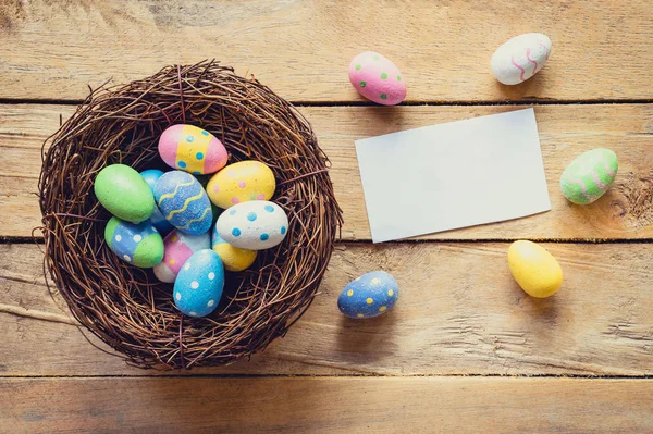 Красочные пасхальные яйца в гнезде и бумажная карточка на фоне дерева wi — стоковое фото