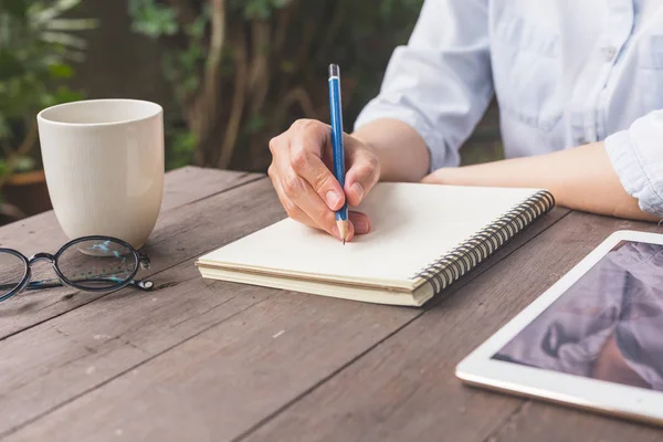 Hand kvinna skriva notebook på trä bord med kopp kaffe och fliken — Stockfoto