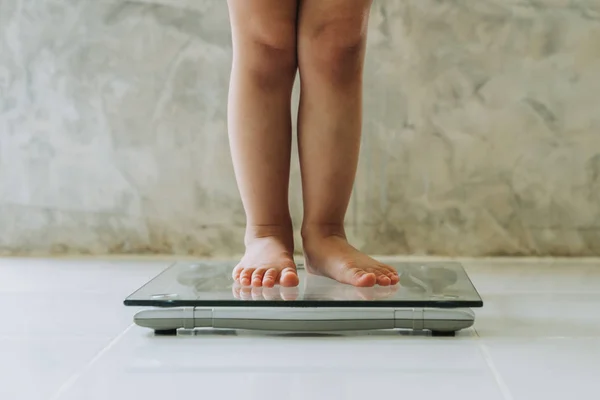 Gadis kecil pada skala berat pada latar belakang lantai, konsep Diet . — Stok Foto