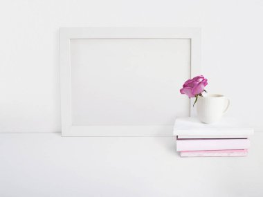 Beyaz boş ahşap çerçeve mockup bir porselen fincan ve yığın kitap masanın üzerinde yatan bir gül çiçek ile. Afiş ürün tasarımı. Stok kadınsı fotoğraf tarz. Ev dekorasyonu.