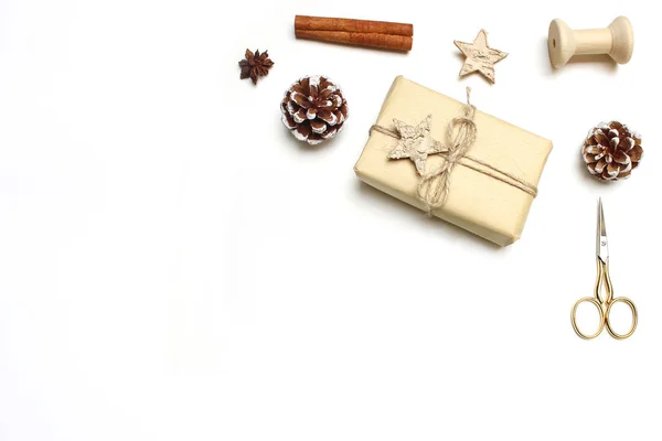 Χριστουγεννιάτικο γιορτινό στυλ εικόνα απόθεμα σύνθεση. Χειροποίητο δώρο κουτί με ξύλινα και αστέρια γλυκάνισο, κανέλα, μπαχαρικό μπαστούνια, pinecones και χρυσή scissorson λευκό φόντο ξύλινη. Το Top view. — Φωτογραφία Αρχείου