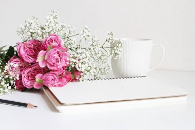 Düğün stok fotoğraf tarz. Pembe Gül, babys nefes Gypsophila çiçekler, beyaz Kupası, kalem ve defter ile natürmort. Çiçek kompozisyon. Görüntü blog ya da sosyal medya için.