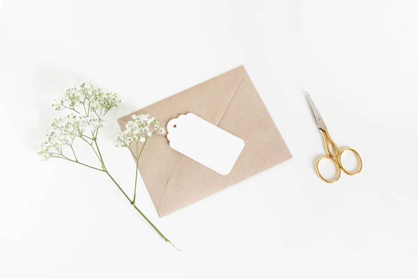 Cartellino regalo bianco con busta di carta artigianale, forbici dorate e alito di babys Fiori di Gypsophila isolati su sfondo bianco del tavolo. Matrimonio o compleanno in stile stock foto, vista dall'alto, lay flat — Foto Stock