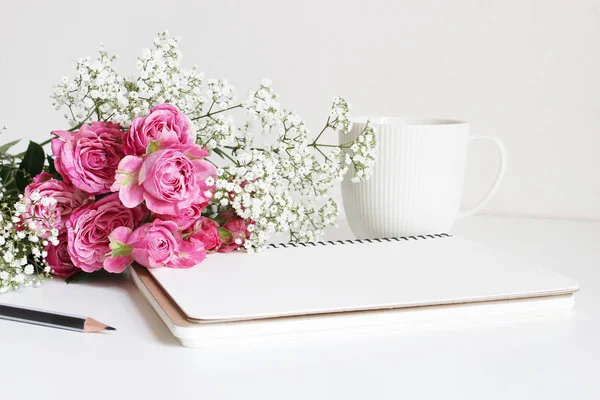 Mariage style photo de stock. Nature morte avec roses roses, souffle de bébé fleurs de Gypsophila, tasse blanche, crayon et carnet. Composition florale. Image pour blog ou médias sociaux . — Photo