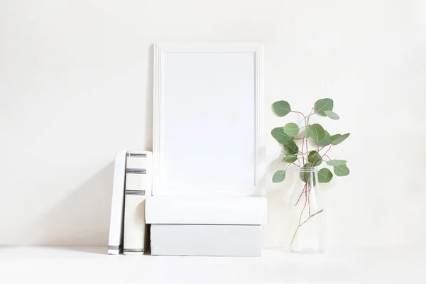 Mockup bianco con cornice in legno bianco con rami di eucalipto verde in bottiglia di vetro e mucchio di libri sdraiati sul tavolo. Poster design del prodotto. Fotografia femminile stock in stile. Arredo casa . — Foto Stock