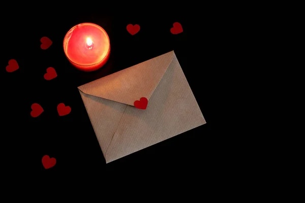 Alla hjärtans dag eller bröllop mock-up scen med öppen craft papper kuvert, papper hjärtan konfetti och brinnande rött ljus på svart bakgrund. Kärlek-konceptet. Platt lekmanna, top view. Tomt utrymme för din text. — Stockfoto