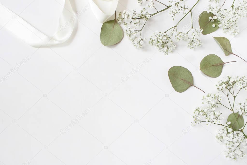 Styled stock photo. Feminine wedding desktop mockup with babys breath Gypsophila flowers, dry green eucalyptus leaves, satin ribbon and white background. Empty space. Top view. Picture for blog.