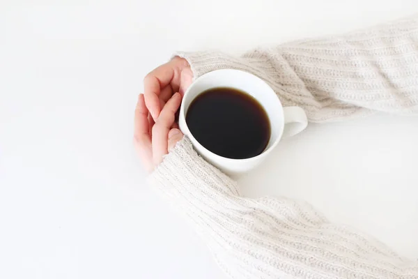 Frauenhände im Pullover halten eine Tasse Kaffee auf einem weißen Tisch. von oben, gestyltes Standbild. Pause, Frühstückskonzept. — Stockfoto