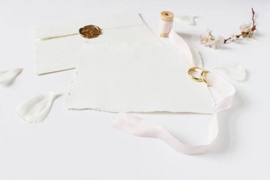 Tebrik kartı düğün, davet iki altın yüzük, kiraz ağacı çiçekleri, beyaz gül yaprakları, biriktirme pembe ipek kurdele ve bir mühür ile el yapımı zarf. Kadınsı stok görüntü tarz.