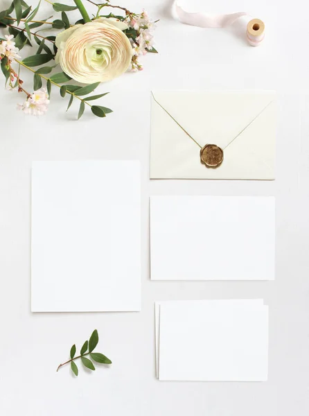 Feminine wedding, birthday desktop mock-ups. Blank greeting cards, envelope. Eucalyptus branches, pink cherry tree blossoms and Persian buttercup flowers. White table background. Flat lay, top view. — Stock Photo, Image