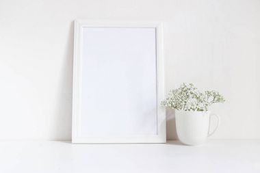 Beyaz boş ahşap çerçeve mockup bebek nefes, porselen kupa masada Gypsophila çiçeklenir. Afiş ürün tasarımı. Stok kadınsı fotoğraf tarz. Ev dekorasyonu.