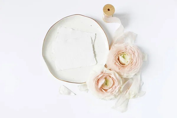 Feminine wedding, birthday desktop mock-up scene. Porcelain plate, blank craft paper greeting cards, silk ribbon, blush pink Persian buttercup flowers. White table background. Flat lay, top view. — Stock Photo, Image