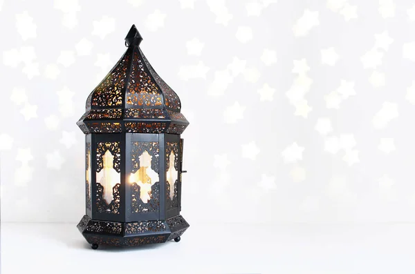 Ornamental dark Moroccan, Arabic lantern on the white table. Burning candle, glittering bokeh lights stars. Greeting card for Muslim community holy month Ramadan Kareem. Festive background. — Stock Photo, Image