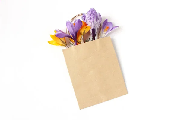 Composizione floreale pasquale. Fiori crochi gialli e viola in carta artigianale shopping bag su sfondo bianco in legno. Scena del mockup primaverile, concetto di business. Posa piatta, vista dall'alto . — Foto Stock