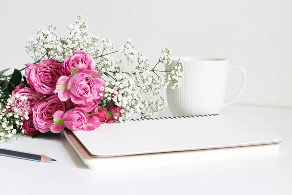 Photo de stock stylisée. Gros plan de bouquet de mariage composé de roses roses et de souffle de bébé, fleurs de Gypsophila couchées sur une table blanche. Nature morte féminine, carnet vierge, crayon et tasse de café blanc . — Photo