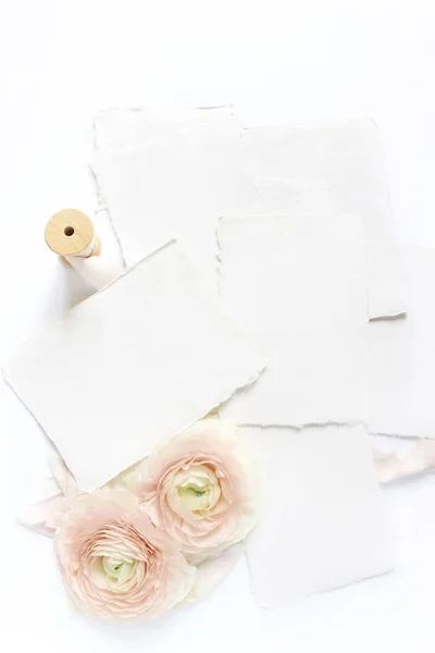 Matrimonio femminile, scena del modellino del desktop di compleanno. Biglietti di auguri in carta bianca artigianale, nastro di seta e fiori di ranuncolo persiano rosa arrossito. Sfondo tavolo bianco. Posa piatta, vista dall'alto . — Foto Stock