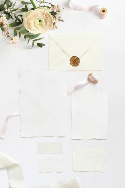 Matrimonio femminile, modelli di desktop di compleanno. Biglietti d'auguri vuoti, busta. Rami di eucalipto, fiori di ciliegio rosa e fiori di ranuncolo persiano. Sfondo tavolo bianco. Posa piatta, vista dall'alto . — Foto Stock