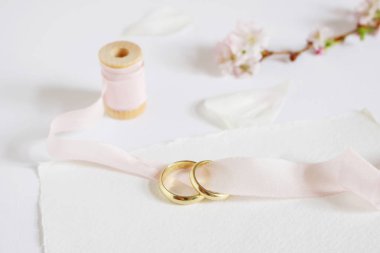 Düğün tebrik kartı, iki altın yüzük, kiraz ağacı çiçekleri, beyaz gül yaprakları ile davet biriktirmek pembe ipek kurdele ve boş kağıt kartı. Kadınsı stok görüntü tarz.