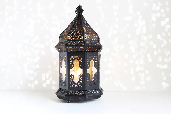 Ornamental dark Moroccan, Arabic lantern on the white table. Burning candle, glittering bokeh lights. Greeting card for Muslim community holy month Ramadan Kareem. Festive background. — Stock Photo, Image