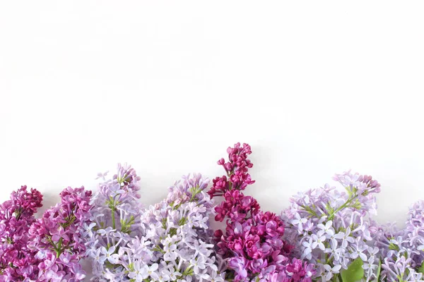 Foto stock in stile. Scena femminile primaverile, composizione floreale. Bandiera decorativa fatta di bellissimi fiori lilla viola. Sfondo tavolo bianco. Posa piatta, vista dall'alto . — Foto Stock