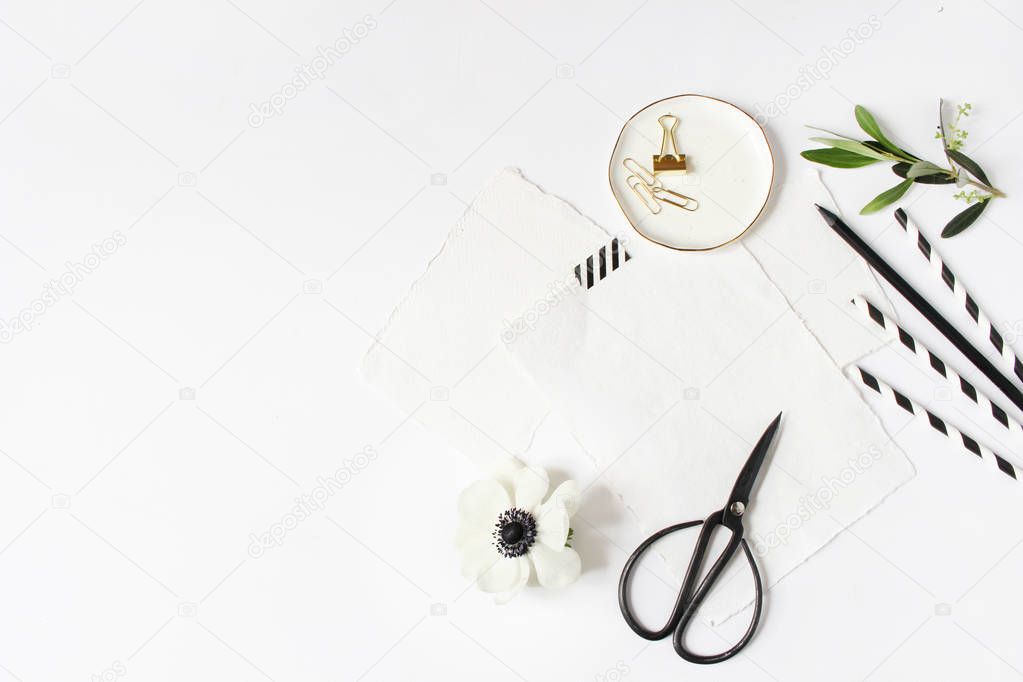 Breakfast or birthday party desktop scene. Composition with empty milk glass jar, black and white drinking paper straws and anemone flower.White table background. Flat lay, top view.