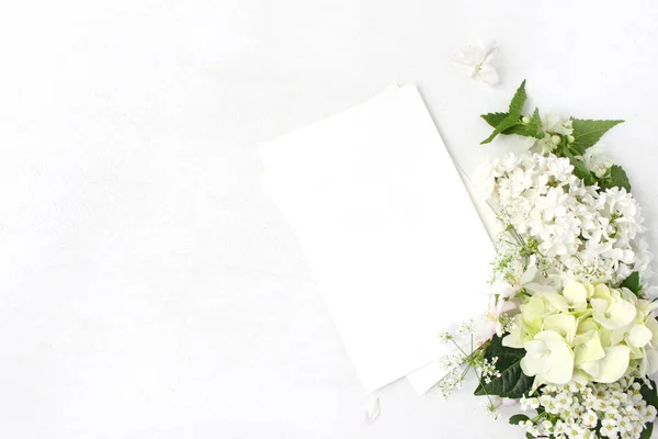 Mockup decorativo, composizione floreale. Matrimonio selvaggio o bouquet di compleanno di ortica bianca in fiore, lilla, ramo di melo, ortensia, fiori di spirea e carte di carta bianca. Posa piatta, vista dall'alto . — Foto Stock