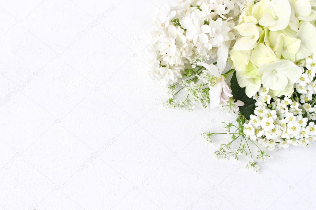 Styled stock photo. Decorative floral composition. Wild wedding or birthday bouquet of blossoming white lilac, apple tree branch, hydrangea, spirea flowers. White table background. Flat lay