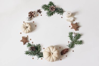 Noel çemberi çiçek kompozisyonu. Köknar ağacı dalları, çam kozalakları, konfeti, tahta yıldızlar, beyaz arka planda beyaz balkabakları. Kış, yeni tasarım ve dekorasyon. Düz yatış, üst görünüm.