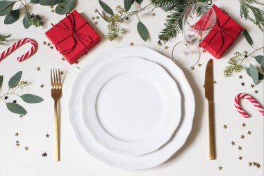 Noel sofrası kurulumu. Altın çatal bıçak takımı, porselen tabaklar, şampanya bardağı, köknar ağacı, okaliptüs dalları, kırmızı hediye kutuları ve altın konfeti yıldızları. Kış tatili geçmişi. Dikey düzlük.
