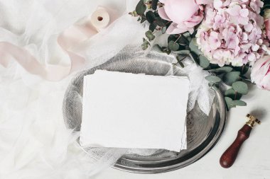 Doğum günü kompozisyonu, kırtasiye malzemeleri. Eski gümüş tepside düğün kartları var. Okaliptüs, pembe güller, ortanca, şakayık çiçekleri, beyaz masa örtüsü ve kurdele. Düz yatıyordu, üst.