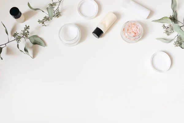 Styled beauty frame, web banner. Skin cream, shampoo bottle, dry eucalyptus leaves and pink Himalayan salt. White table background. Organic cosmetics, spa concept. Empty space, flat lay, top view. — Stockfoto