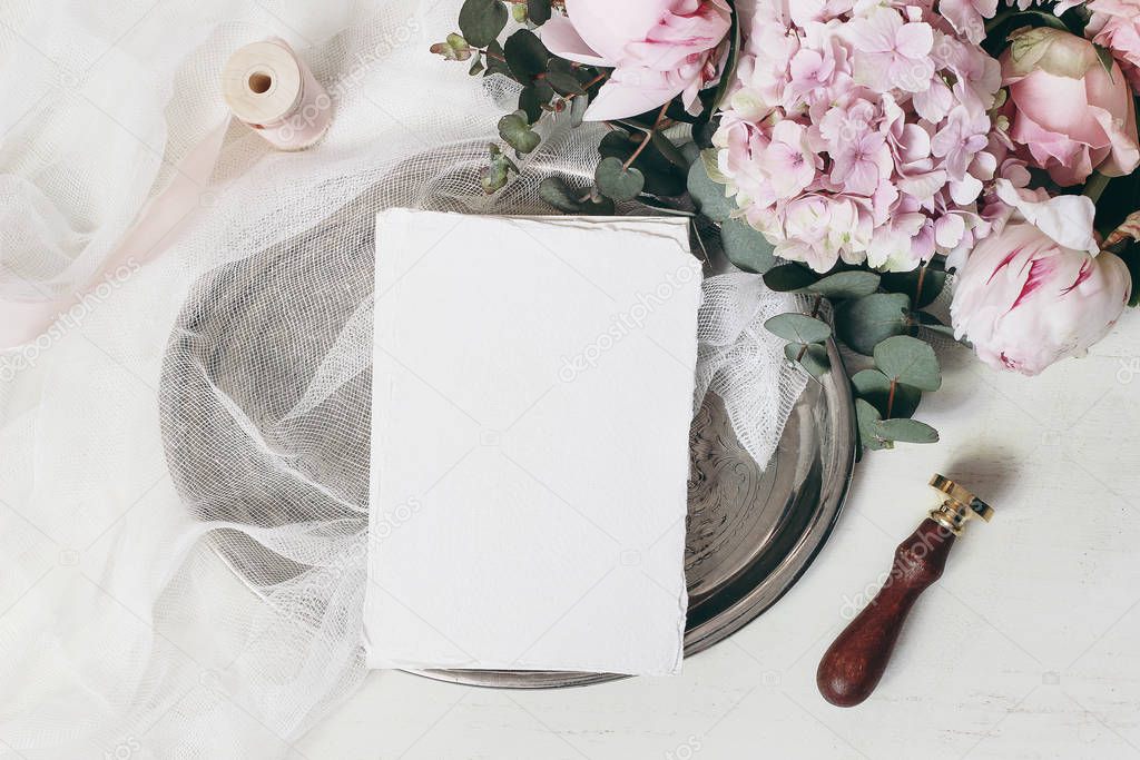 Wedding, birthday composition, stationery mockup scene. Greeting cards on old vintage silver tray. Eucalyptus, pink roses, hydrangea, peony flowers, seal stamp on white table. Flat lay, top view.
